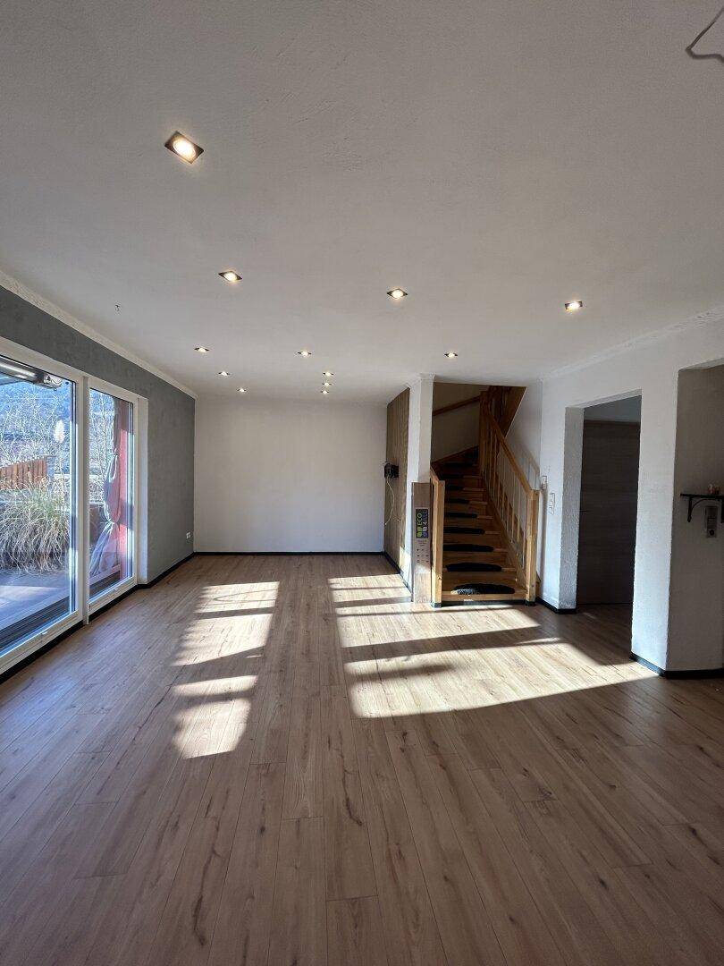 Geräumiger Wohnbereich mit Laminatboden, Holztreppe und direktem Zugang zur sonnigen Außenterrasse.
