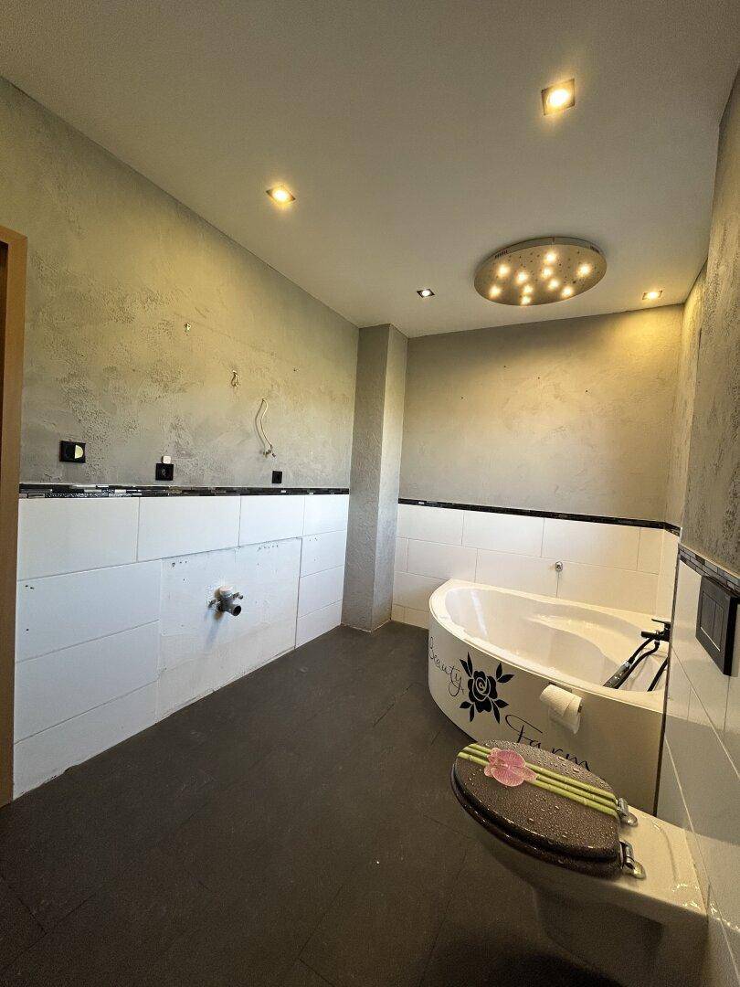 Renovierungsbedürftiges Badezimmer mit Eckbadewanne, wandhängendem WC und vorbereitetem Waschtischbereich.