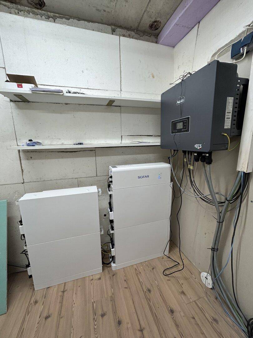 Unfertiger Technikraum mit Solaranlage und Batteriespeicher auf Holzboden.