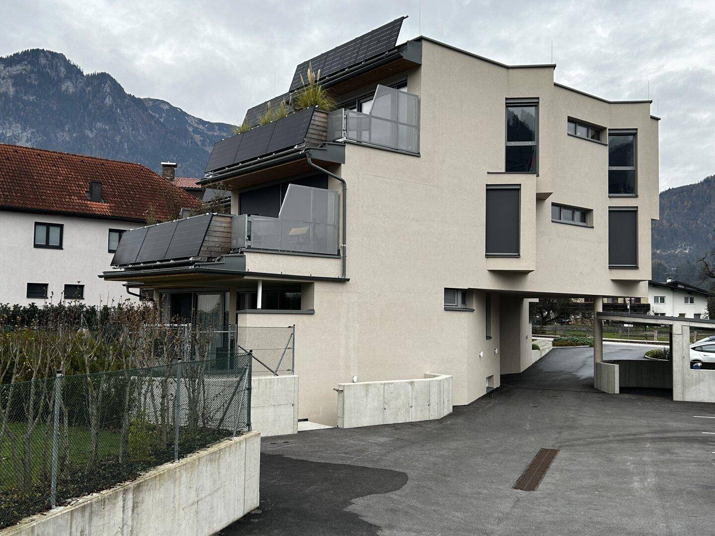 Moderne Wohnanlage mit Balkonen, Solarpaneelen und Bergblick unter bewölktem Himmel.