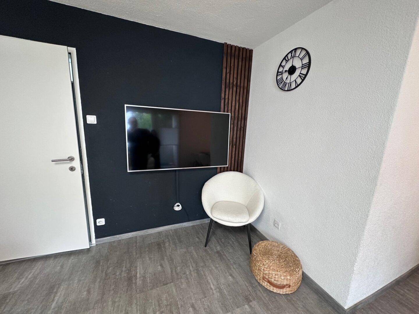 Moderner Wohnbereich mit wandmontiertem Fernseher an einer dunklen Akzentwand.