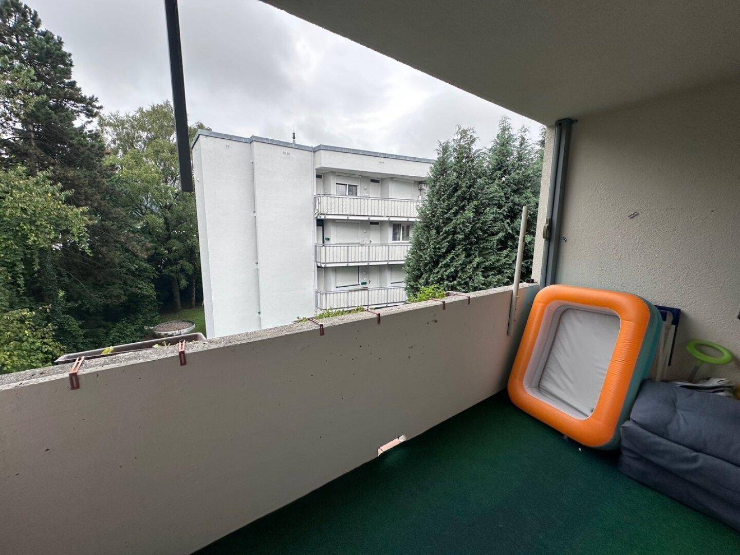 Balkon mit Blick auf umliegende Gebäude und viel Grün, ausgestattet mit einem kleinen Planschbecken.