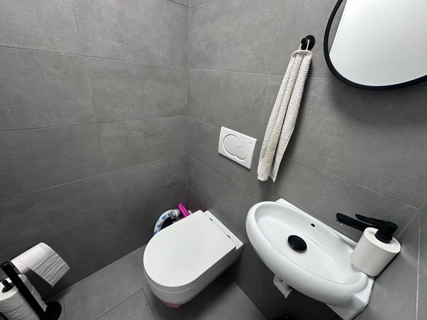 Kleines Gäste-WC mit modernen grauen Fliesen, wandhängendem WC und Handwaschbecken.