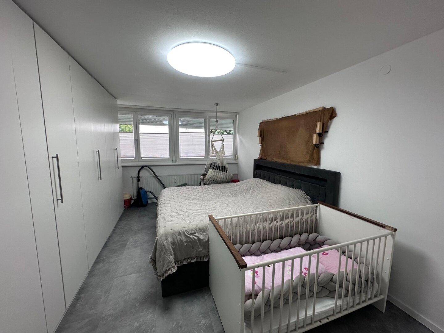 Schlafzimmer mit Doppelbett, Babybett und praktischen Einbauschränken entlang der Wand.