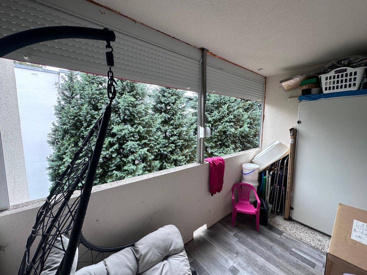 Verglaste Loggia mit Hängesessel und Blick auf hohe Nadelbäume, genutzt als Stauraum.