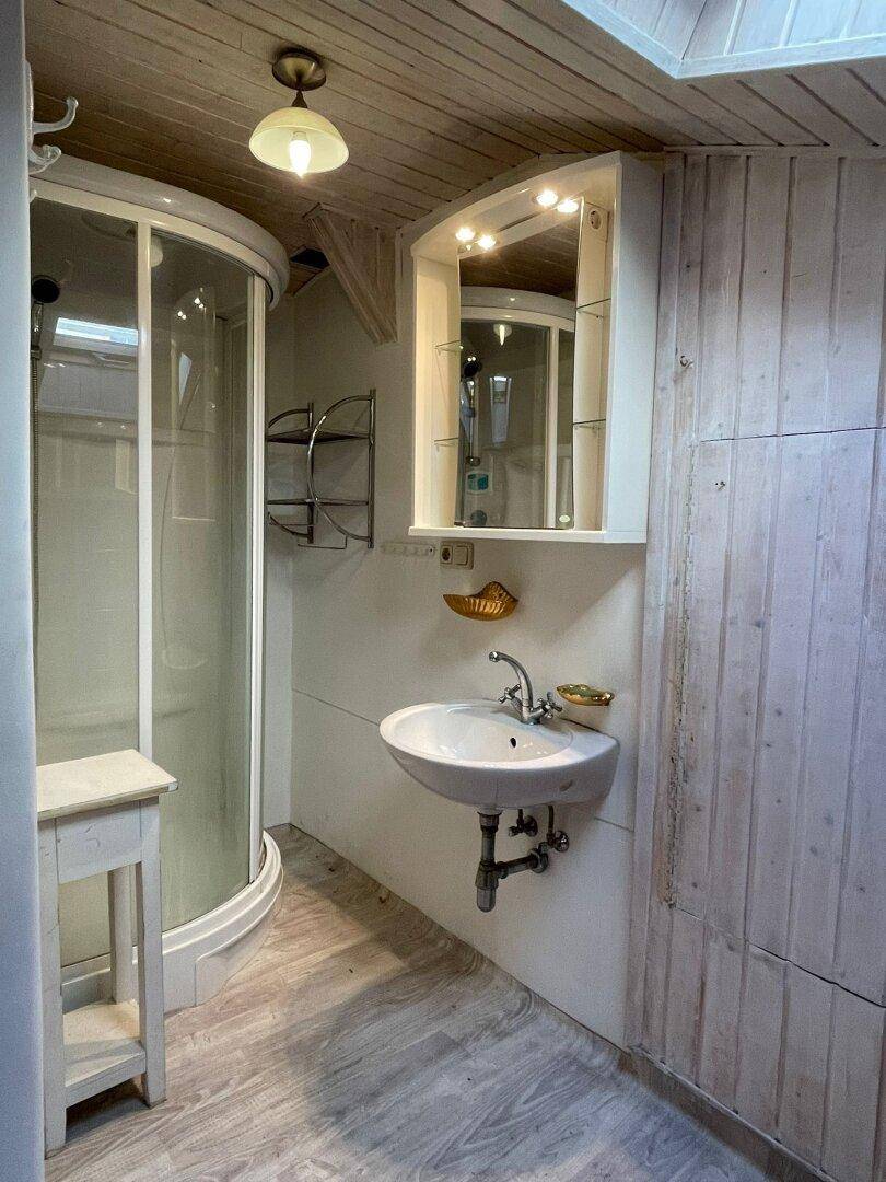 Badezimmer mit Eckdusche, Waschbecken, Spiegelschrank und Holzwänden unter einem Dachfenster.