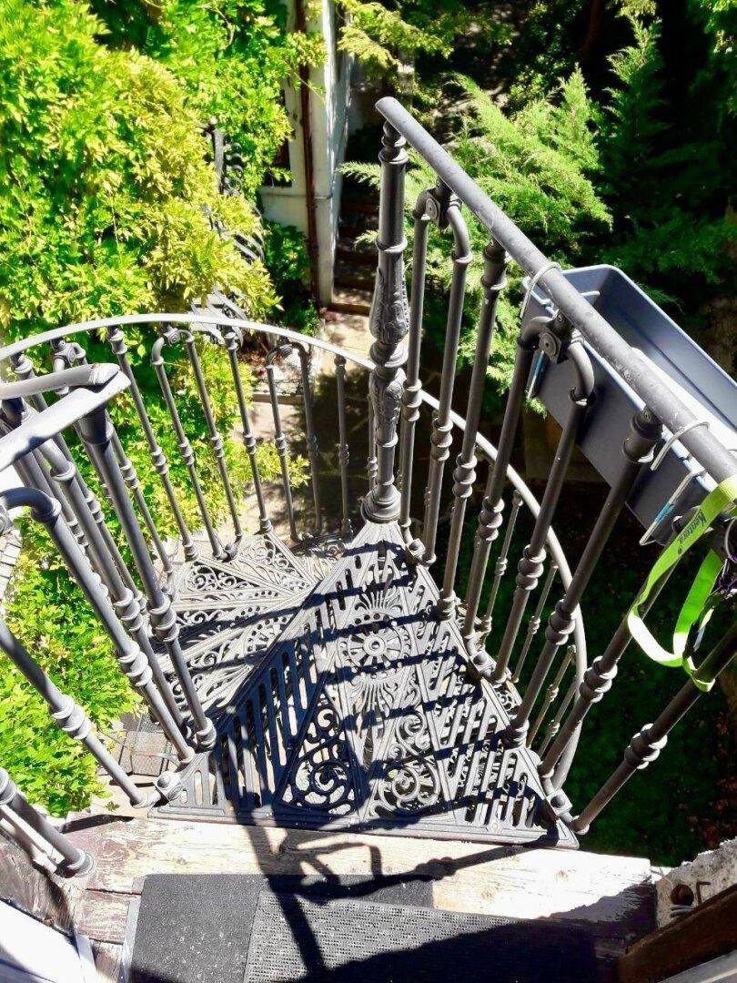 Elegante schmiedeeiserne Wendeltreppe im Außenbereich, umgeben von üppigem Grün.
