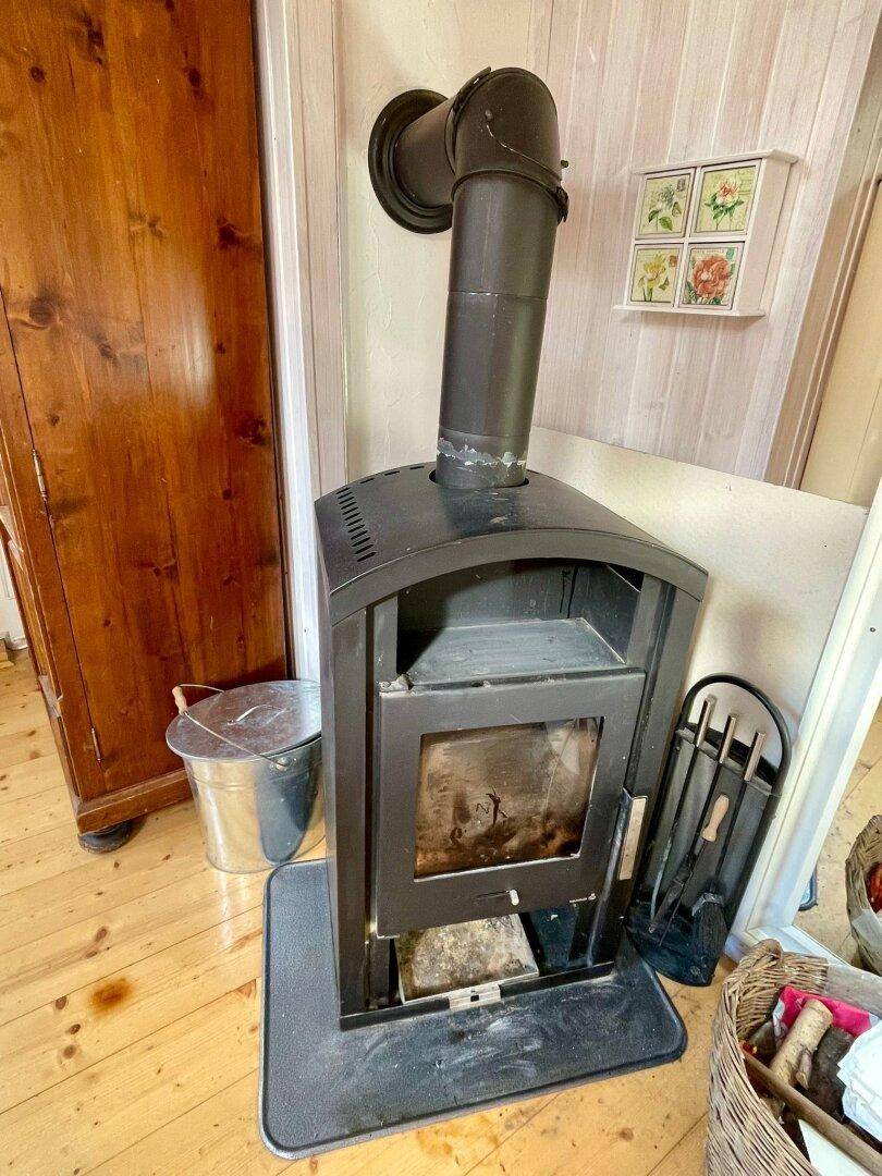 Detailaufnahme eines schwarzen Kaminofens mit Holzscheiten und Zubehör im Wohnbereich.