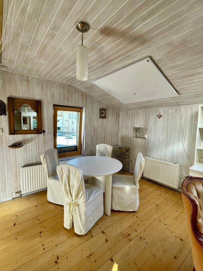Heller Essbereich mit rundem Tisch, weißen Stühlen, Holzwänden und einem Fenster.