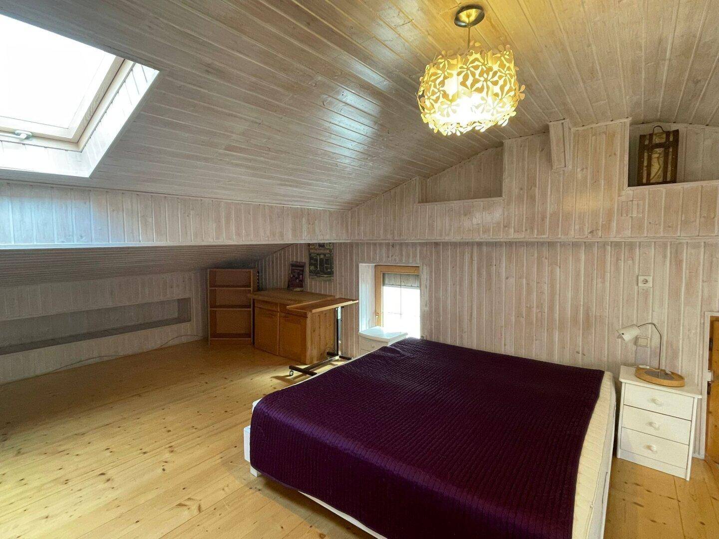 Schlafzimmer unter dem Dach mit Holzboden, Dachschrägen, Dachfenster und einem kleinen Schreibtisch.