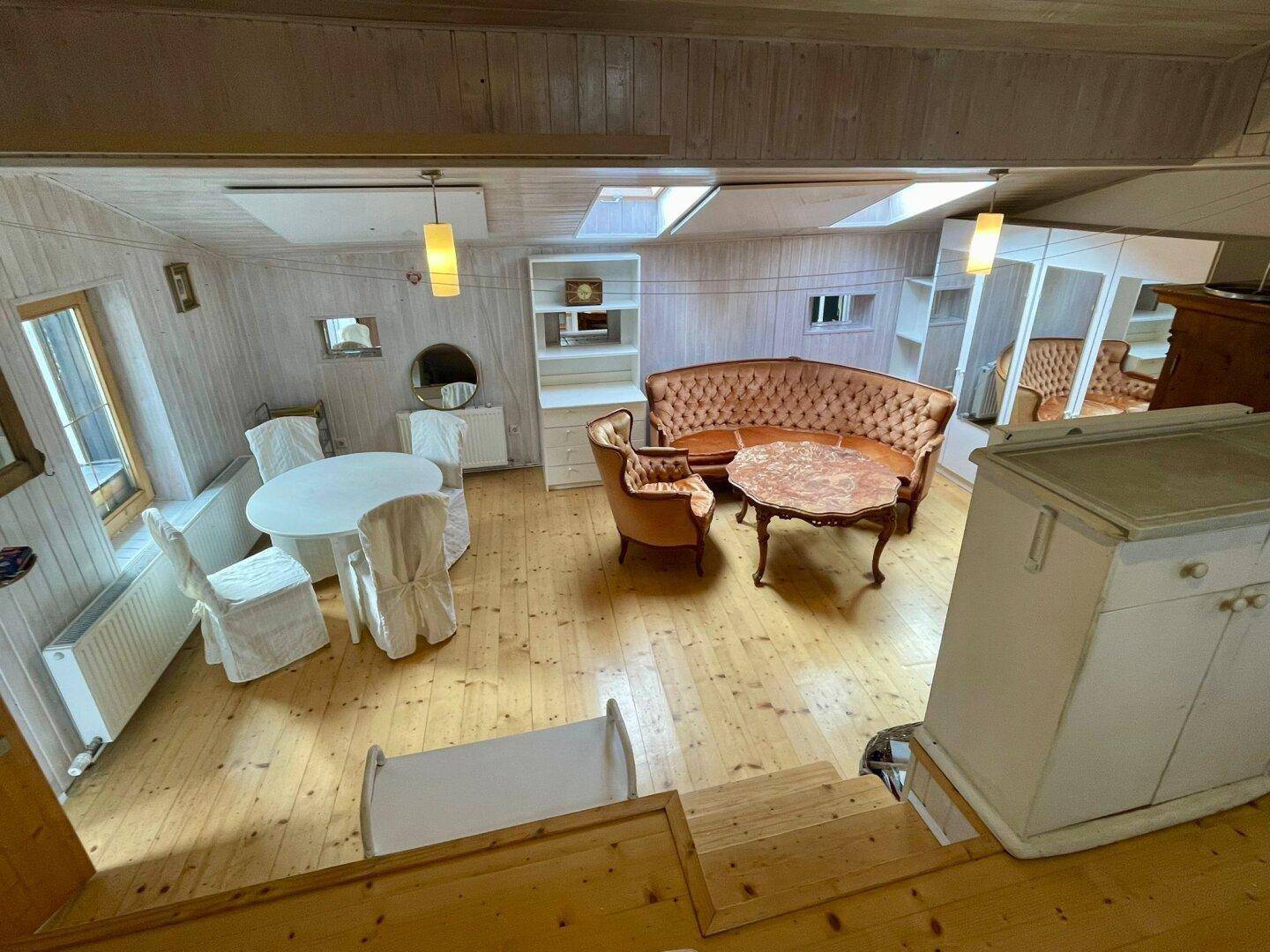 Heller Wohn- und Essbereich mit Holzboden, Dachschrägen und gemütlichen Sitzgelegenheiten.