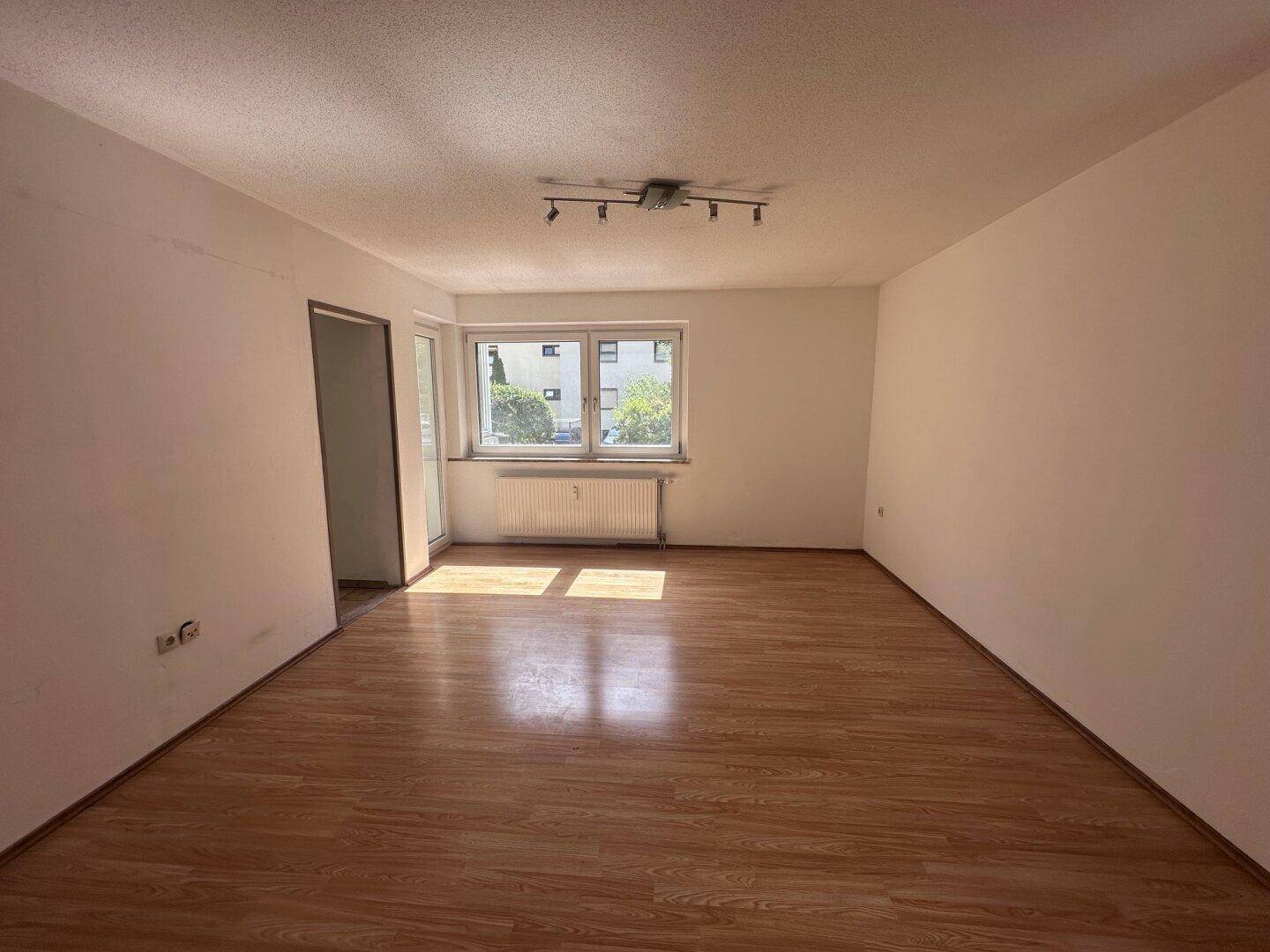Geräumiges Wohnzimmer mit Laminatboden und Zugang zu einem Balkon oder einer Loggia.