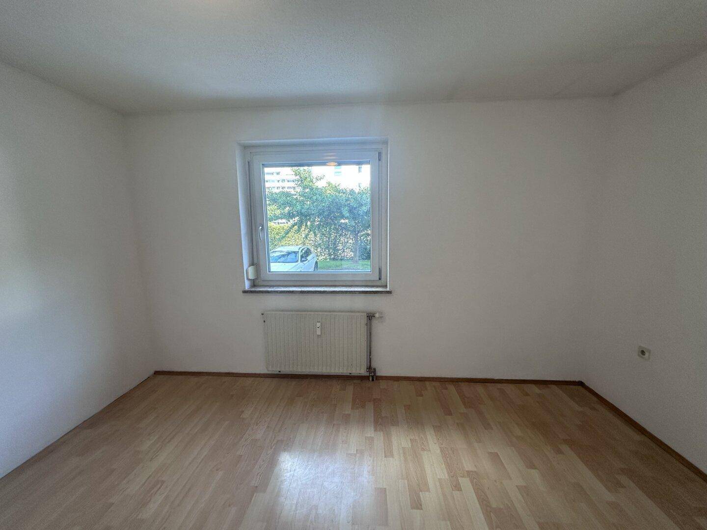 Helles Zimmer mit Laminatboden und einem Fenster mit Blick ins Grüne.