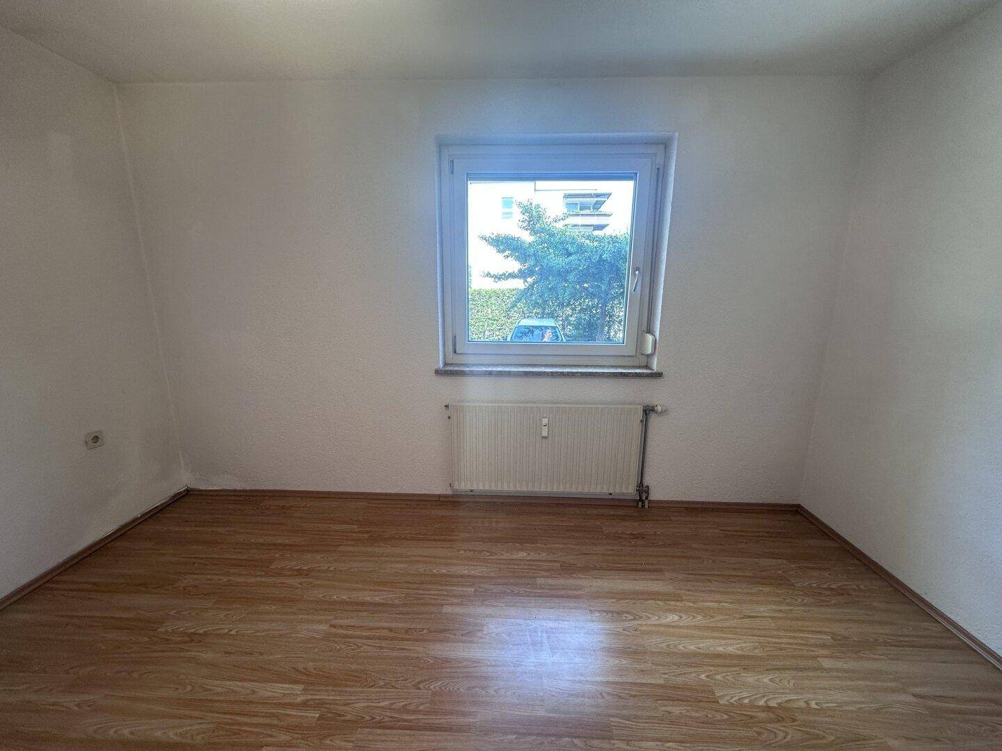 Schlafzimmer mit Laminatboden und einem großen Fenster, das viel Licht spendet.
