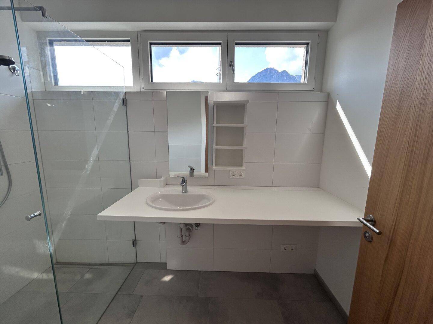Modernes Badezimmer mit weiß gefliesten Wänden, Einzelwaschbecken und Fenstern für Tageslicht.