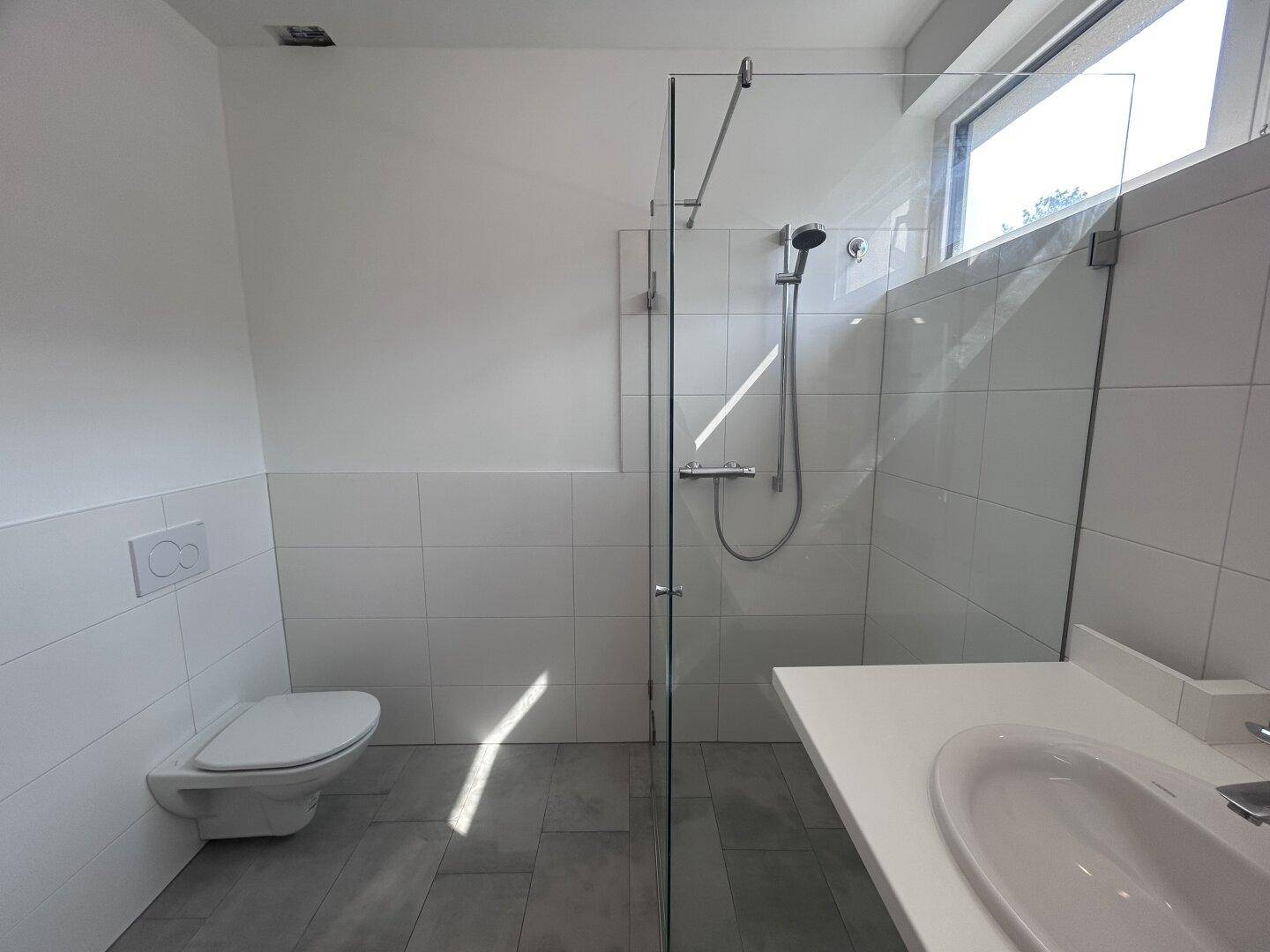 Zeitgemäßes Badezimmer mit wandhängendem WC und einer geräumigen begehbaren Dusche.