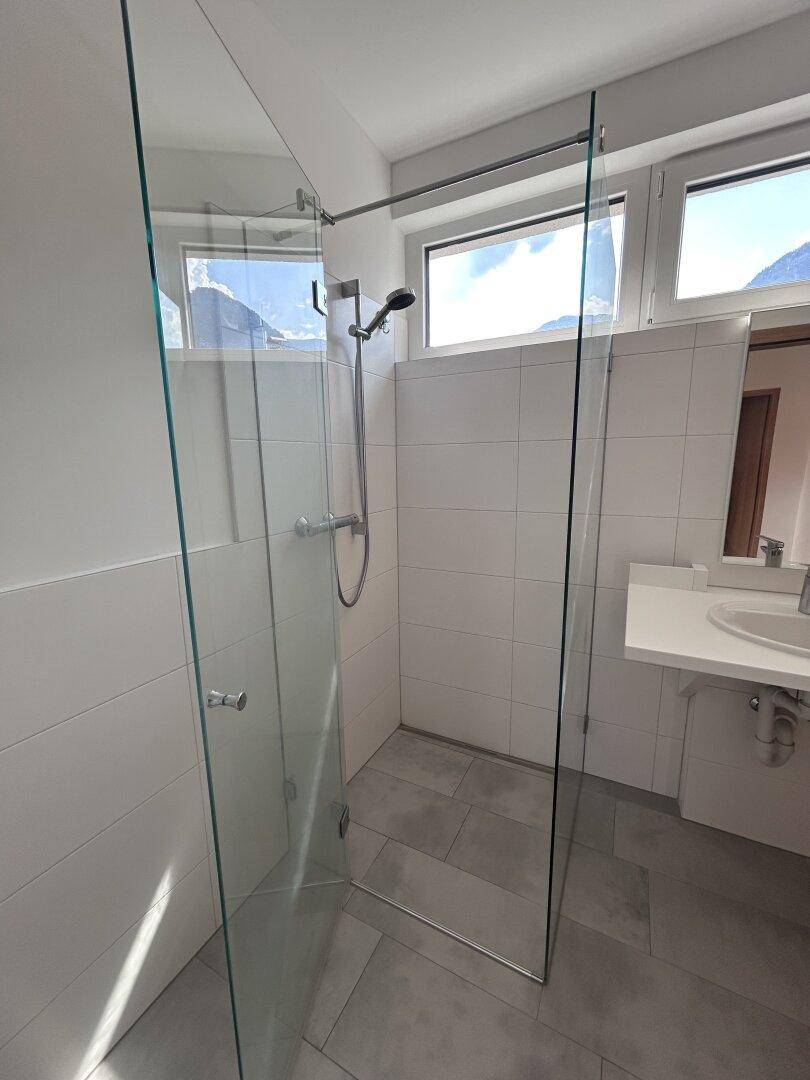 Modernes Badezimmer mit ebenerdiger Glasdusche, Fenster und Bergblick, ausgestattet mit hochwertigen Fliesen.