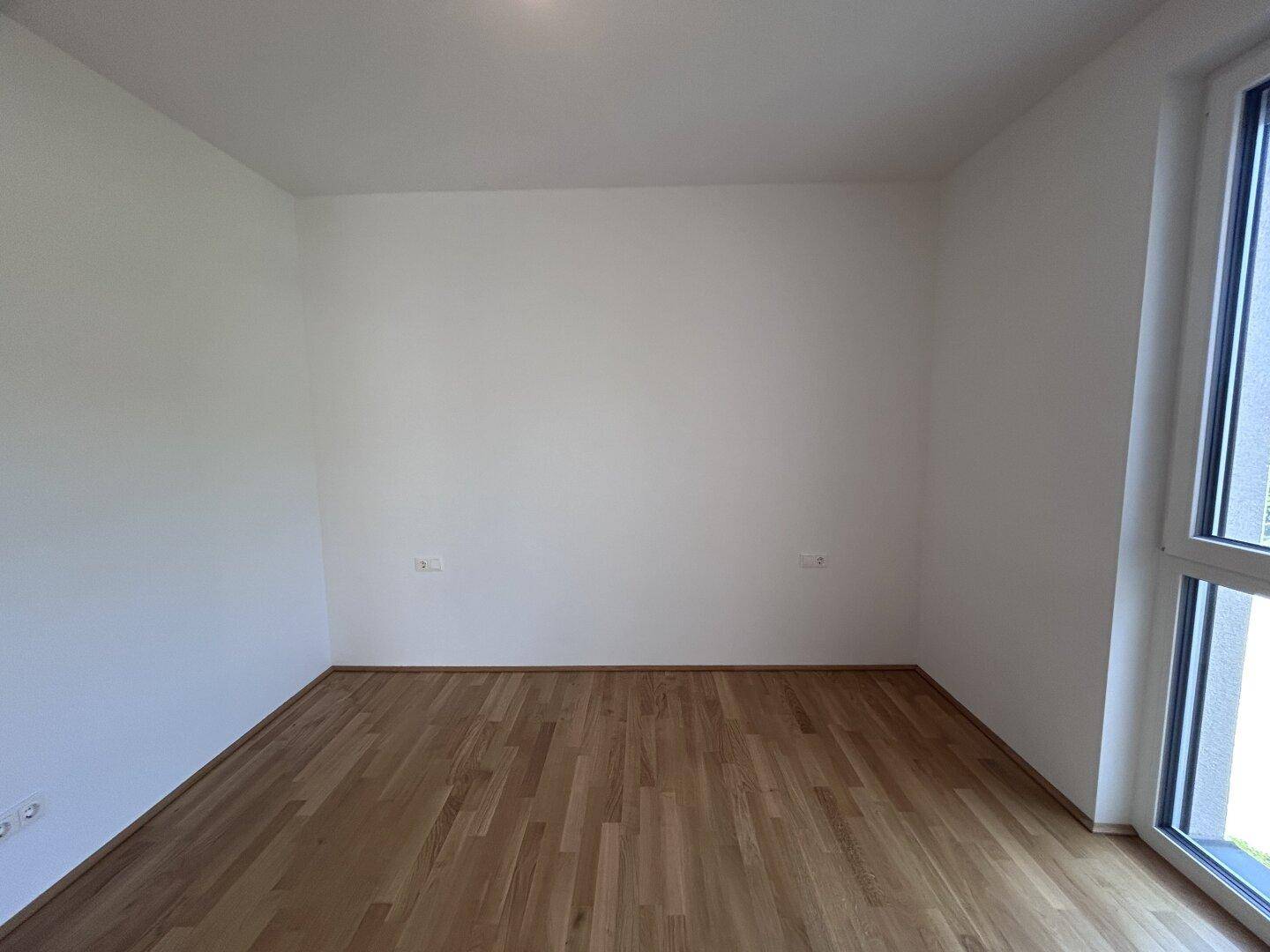 Leeres Zimmer mit hellem Holzparkettboden und weißen Wänden, bereit zur individuellen Gestaltung.