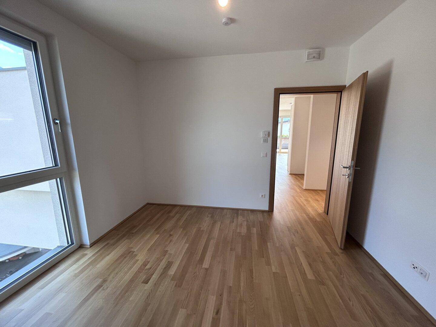 Freundliches Zimmer mit Holzparkett und Zugang zu weiteren Räumen der Wohnung.