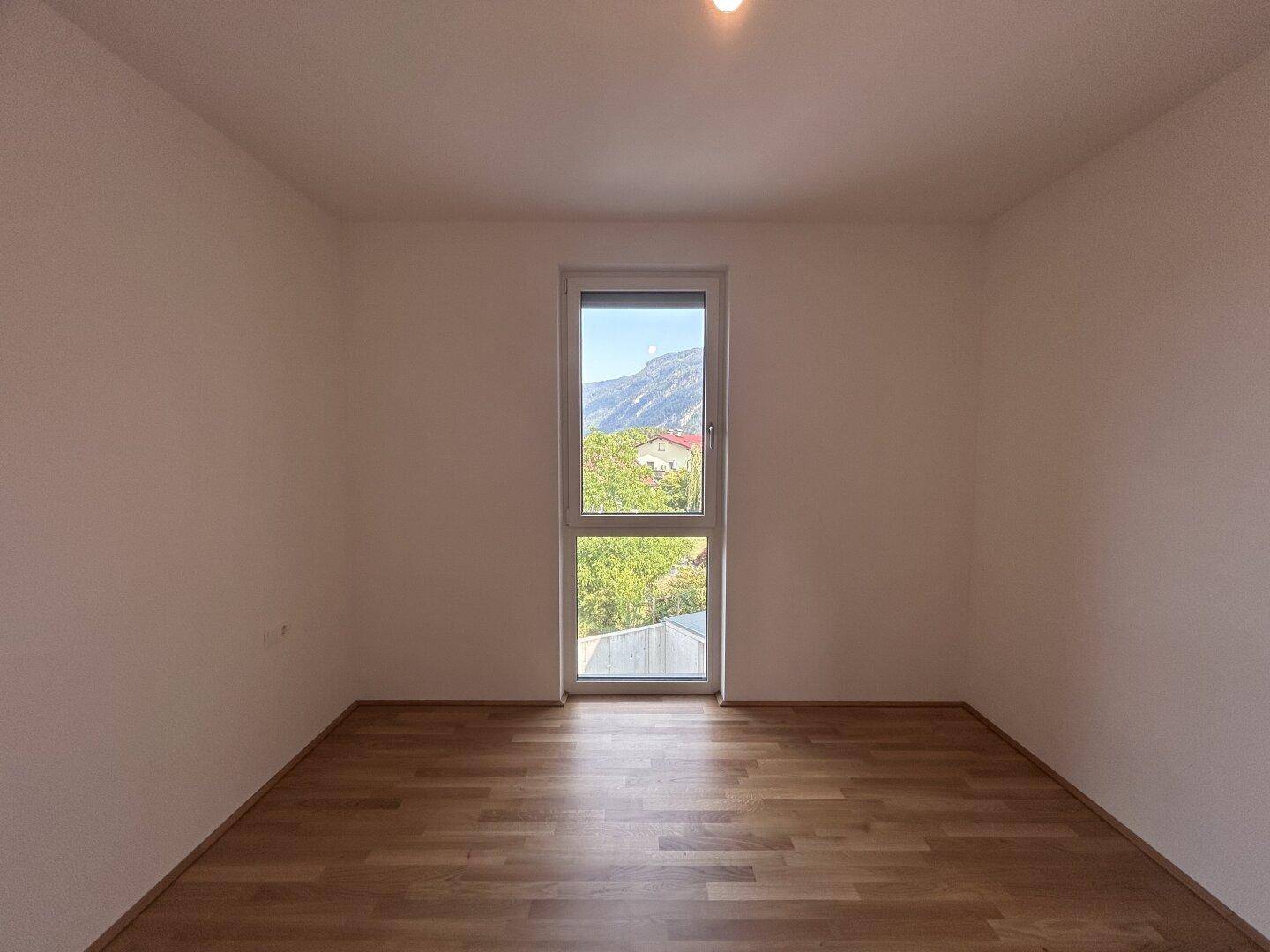 Helles Schlafzimmer mit Holzparkettboden und einem Fenster mit Blick auf die Berge.