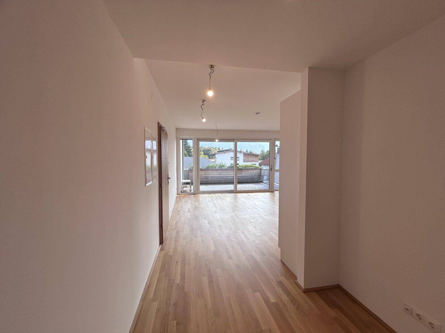 Heller Flur mit Holzparkettboden, der in einen offenen Wohnbereich mit Terrassenzugang führt.