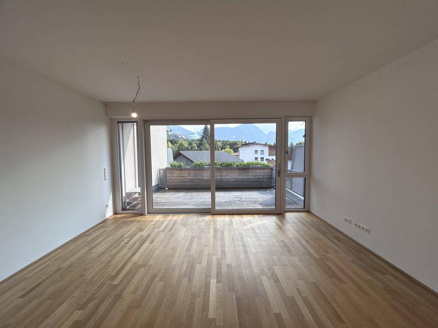 Geräumiges Wohnzimmer mit Holzparkett, großen Schiebetüren zur Terrasse und Bergblick.