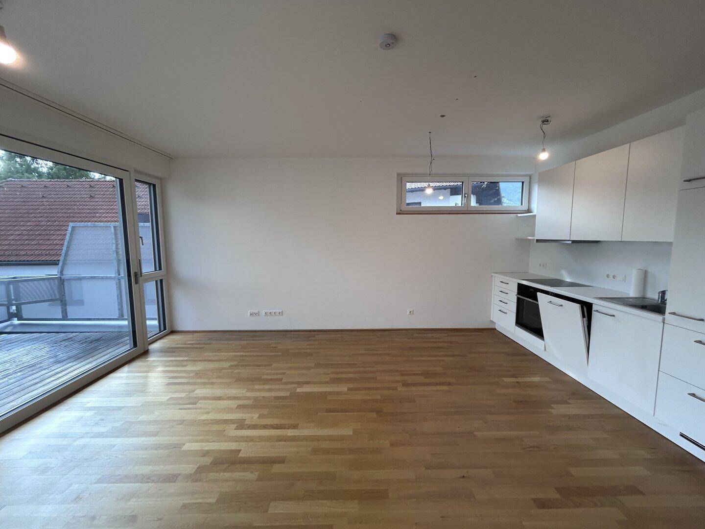 Moderne weiße Einbauküche in einem offenen Raum mit Zugang zu einer sonnigen Terrasse.
