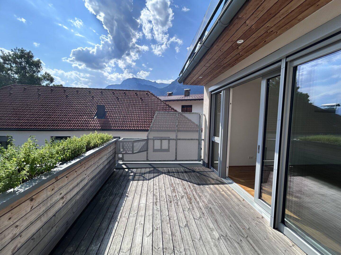 Geräumige Holzterrasse mit Schiebetüren zum Innenbereich und Panoramablick auf die Berge.