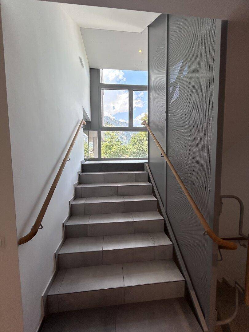 Modernes Treppenhaus mit Holzhandläufen und großen Fenstern, die den Raum erhellen.