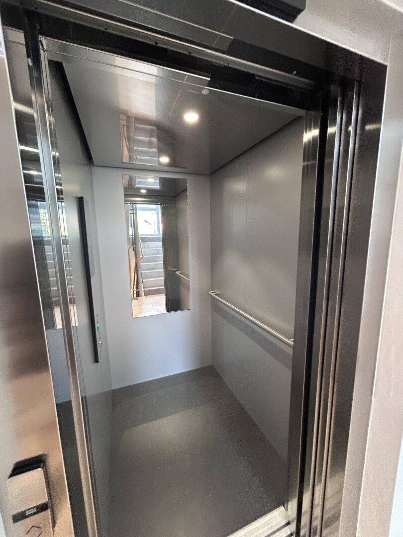 Moderner Aufzug mit Edelstahloberflächen und einem Spiegel im Inneren der Kabine.
