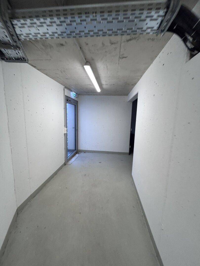 Heller Kellerflur mit Betonwänden und -boden, der zu einem Ausgang führt.