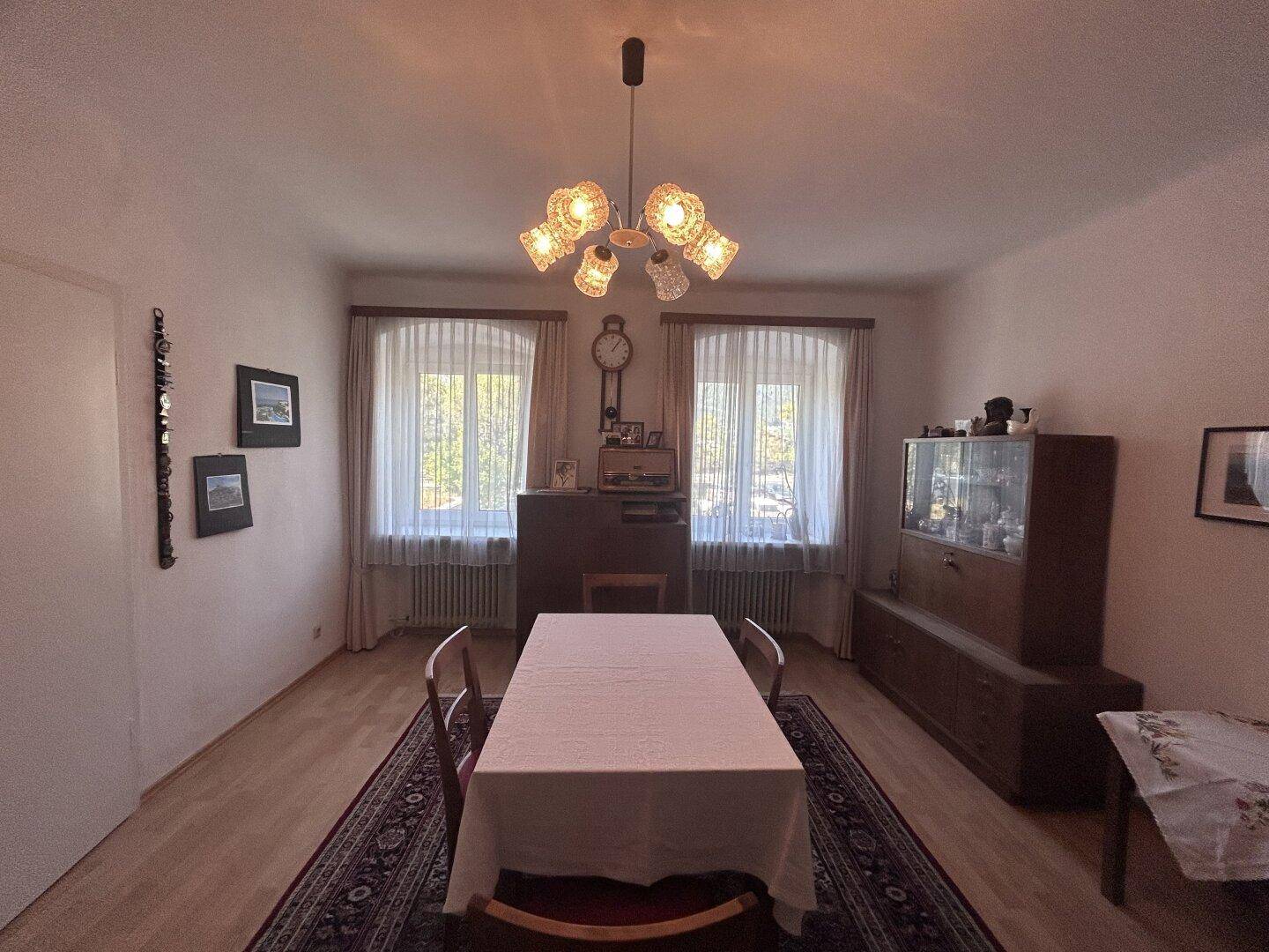 Geräumiges Esszimmer mit großem Esstisch, Teppich und zwei Fenstern für natürliches Licht.