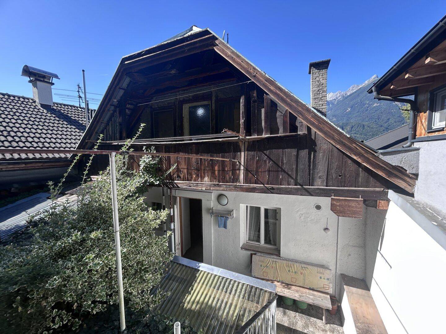 Rückansicht des Gebäudes mit alter Holzfassade und Blick auf die umliegenden Berge.