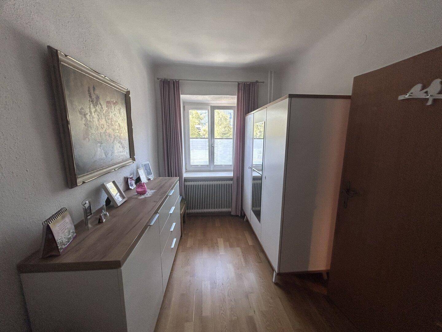 Schlafzimmer mit Holzboden, einem Bett und einem weißen Kleiderschrank, hell durch das Fenster.