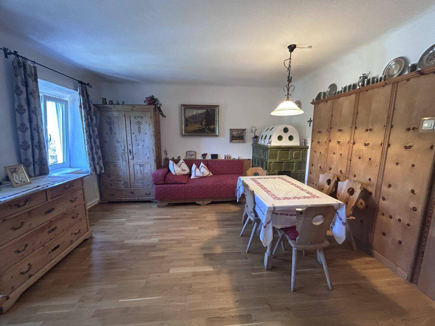Traditioneller Wohn-Essbereich mit Kachelofen, Holzboden und rustikalen Holzschränken.