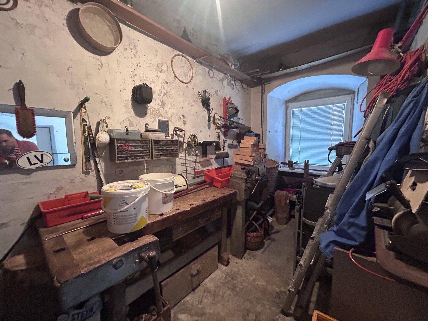 Werkstatt im Kellergeschoss mit Werkbank, verschiedenen Werkzeugen und einem kleinen Fenster.