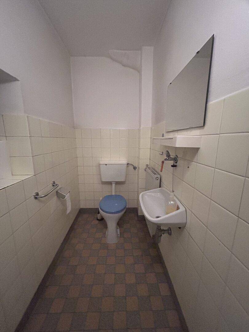 Separates WC mit Toilette, kleinem Waschbecken und halbhoch gefliesten Wänden.