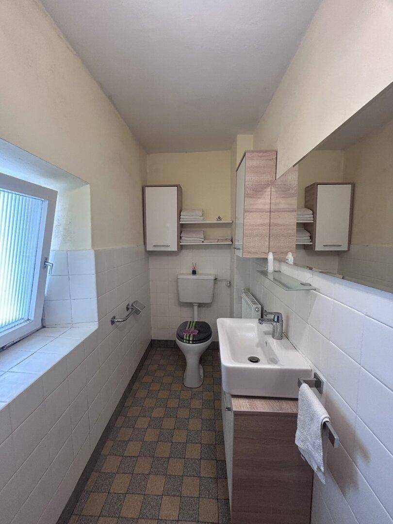 Modernisiertes WC mit Fenster, neuem Waschbeckenunterschrank und halbhoch gefliesten Wänden.