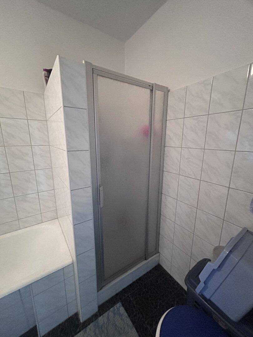 Badezimmer mit Duschkabine, Badewanne und hellen Fliesen im Standardzustand.