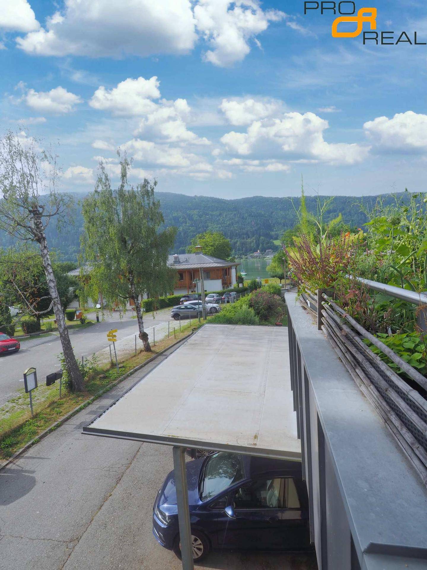 Ausblick von der Immobilie mit Carport, Straße und See- sowie Berglandschaft im Hintergrund.