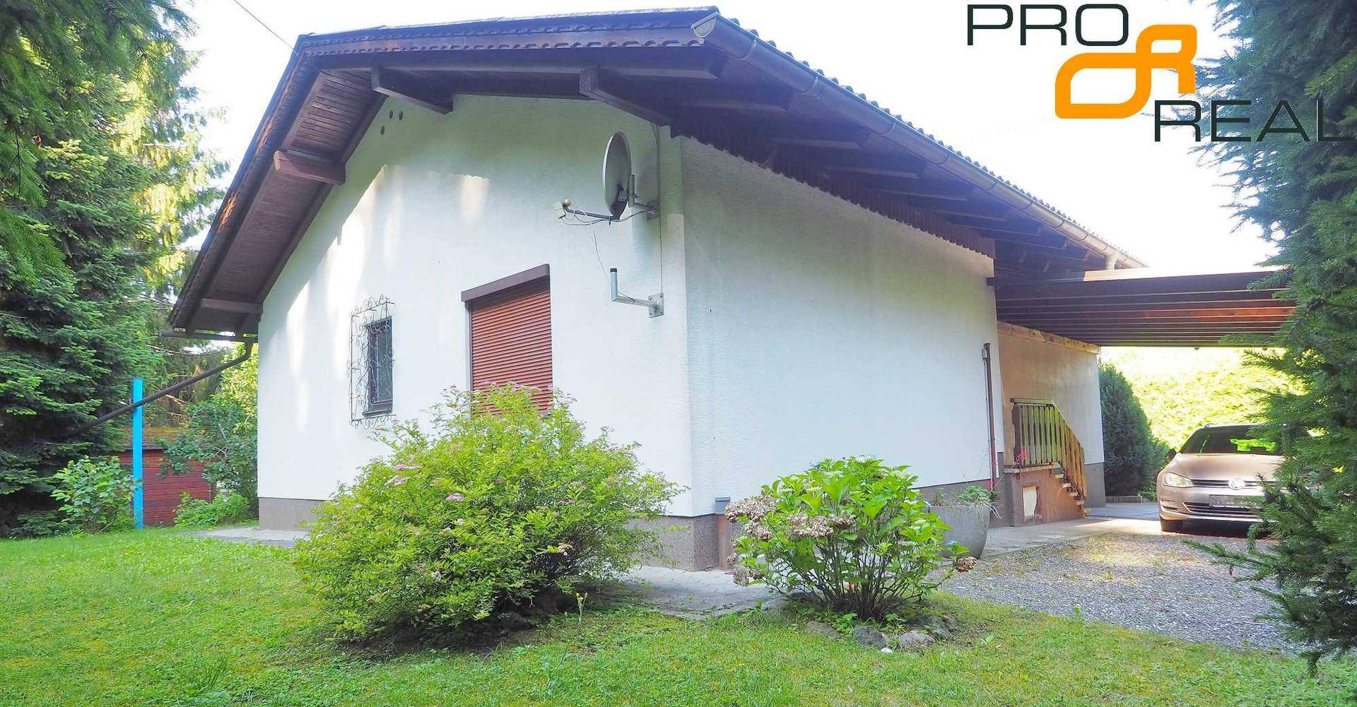 Ansicht des Hauses mit Carport und Zufahrt, umgeben von Bäumen und Sträuchern.