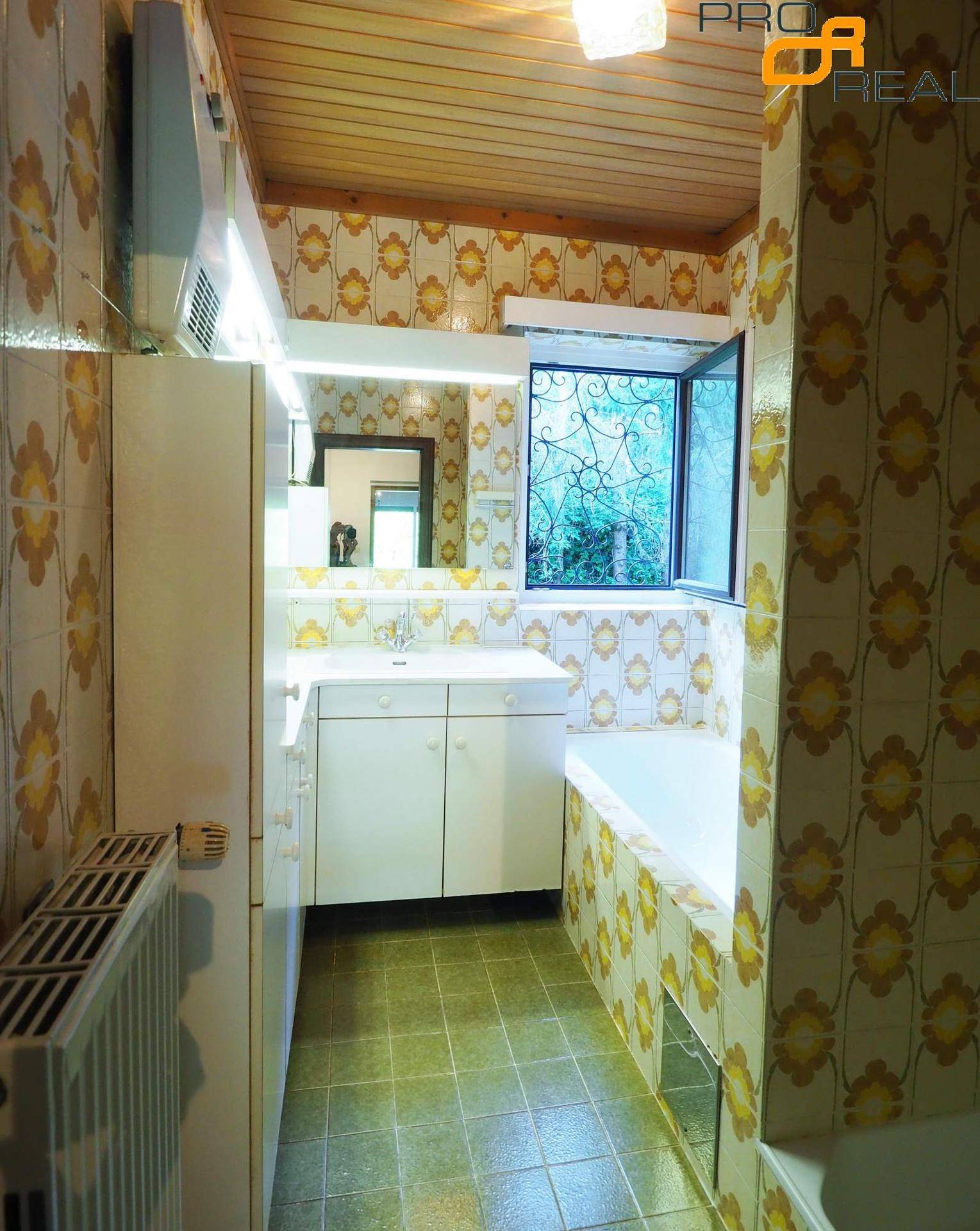 Badezimmer mit Badewanne, Fenster und auffälligen gelb-braunen Fliesen im 80er-Jahre-Stil.