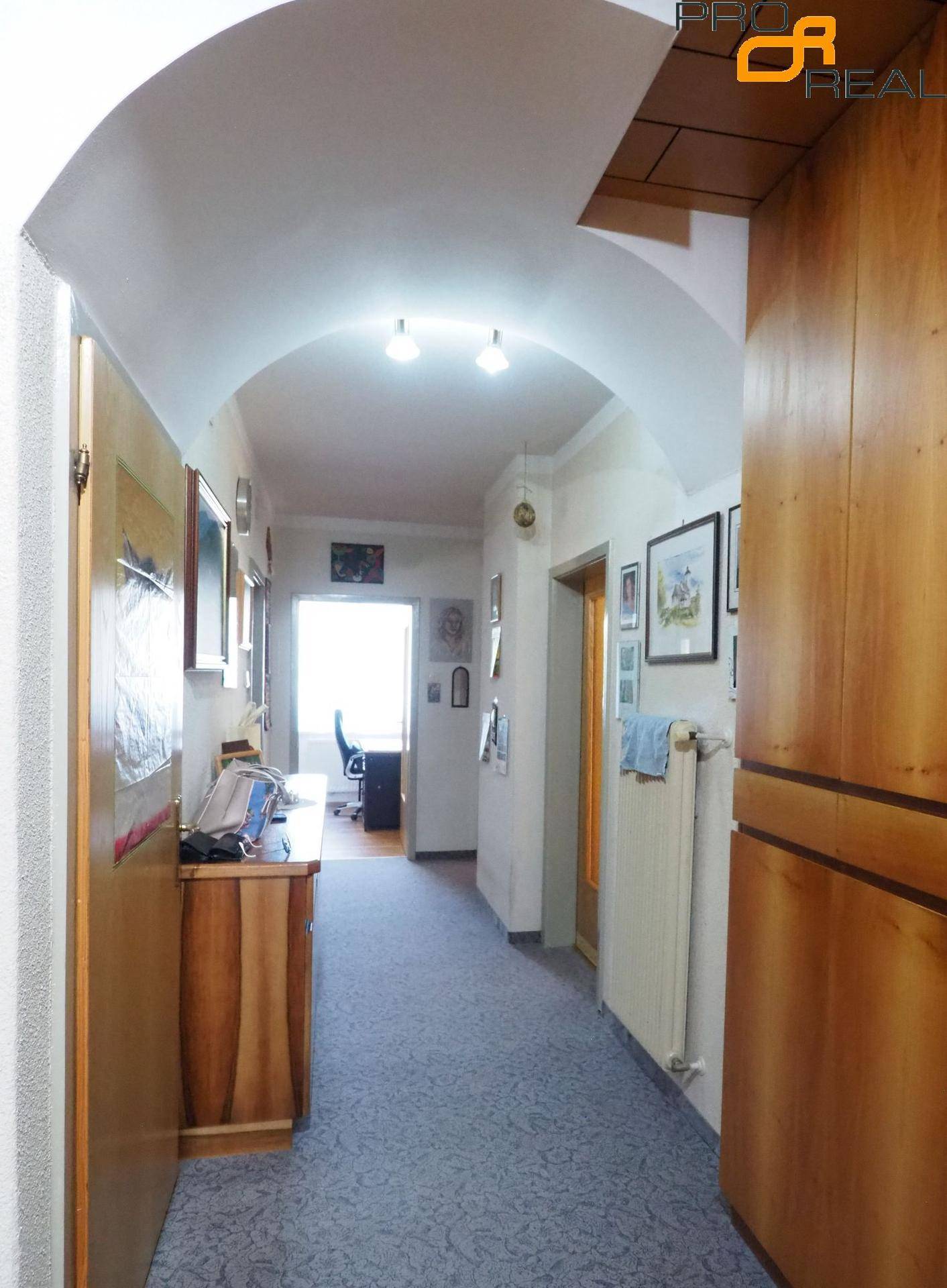 Langer Flur mit Teppichboden, gewölbter Decke und Blick in ein weiteres Zimmer.