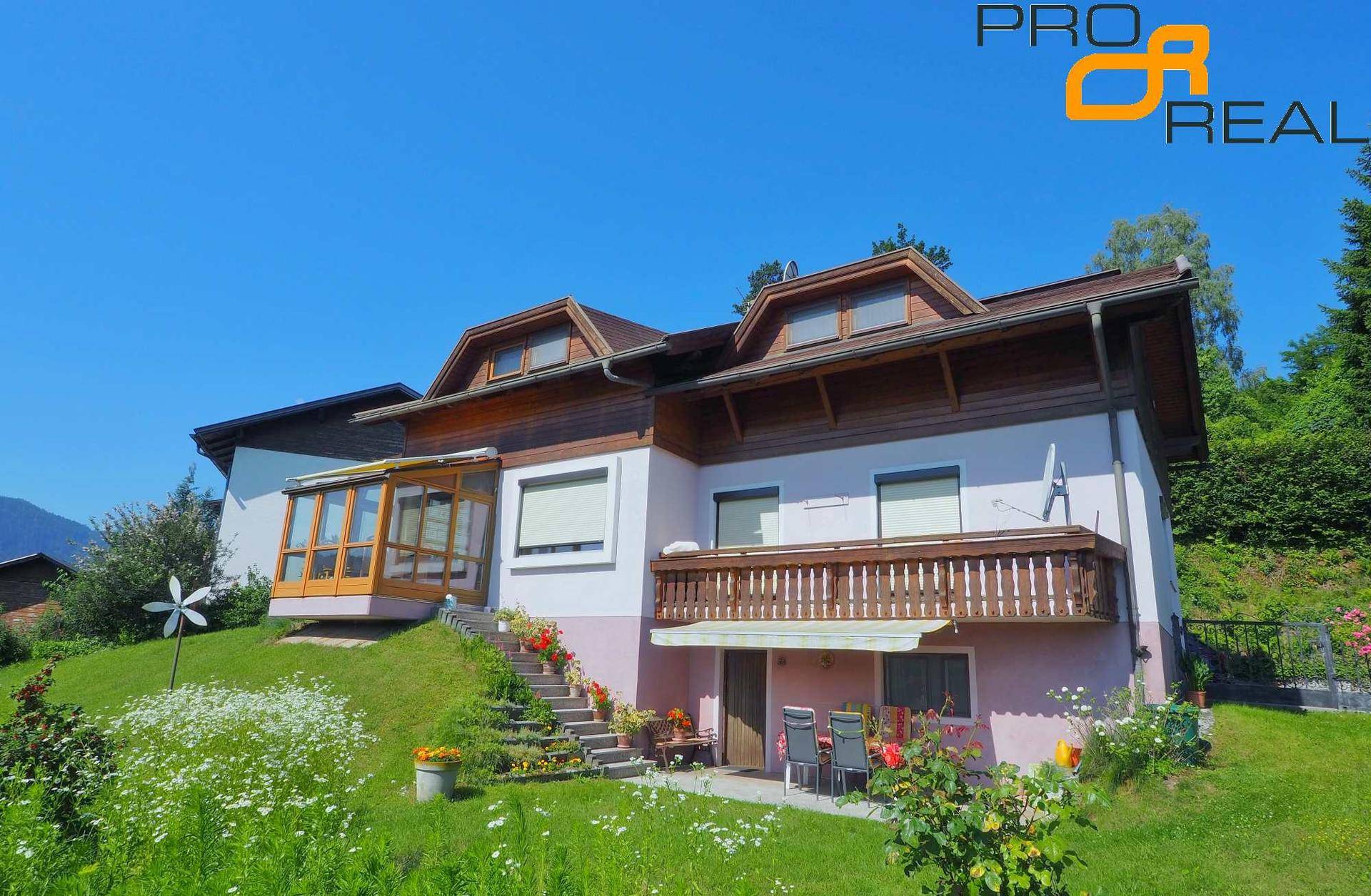 Charmantes Haus mit Balkon, Terrasse und Wintergarten, umgeben von einem grünen Garten.