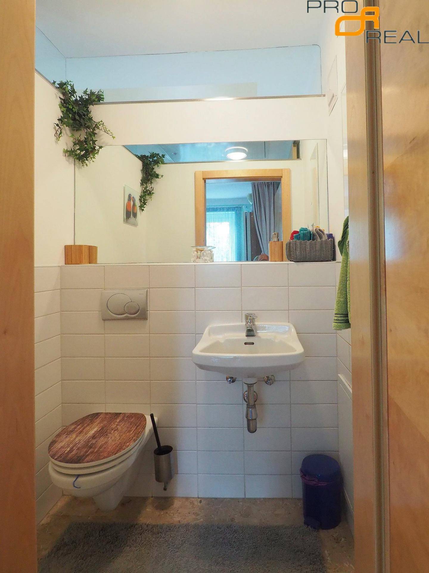 Helles Gäste-WC mit weißen Fliesen, einem Waschbecken und einer Toilette mit Holzdeckel.