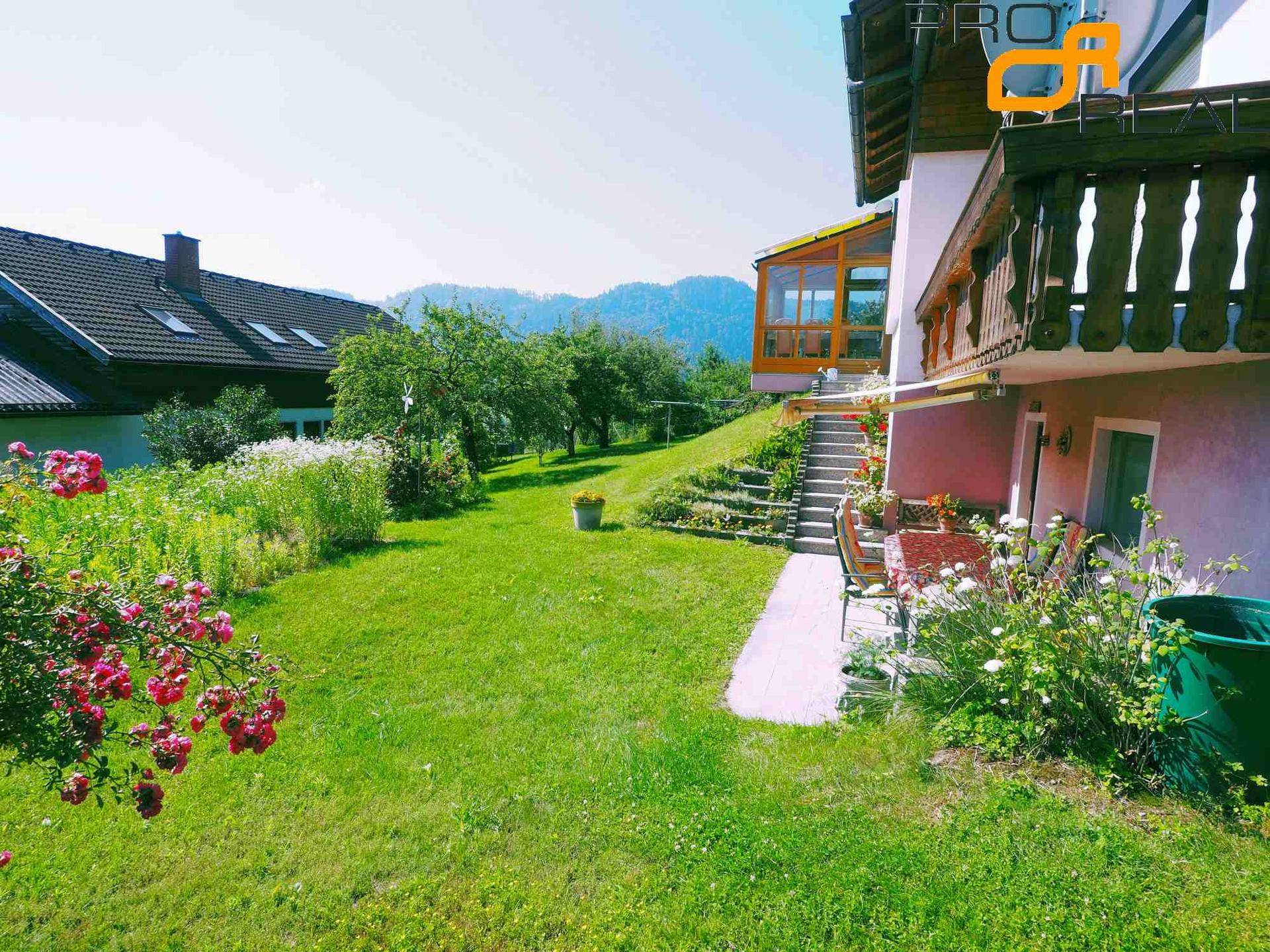 Großer Garten mit Rasenfläche, Blumenbeeten und Blick auf die umliegende Landschaft.