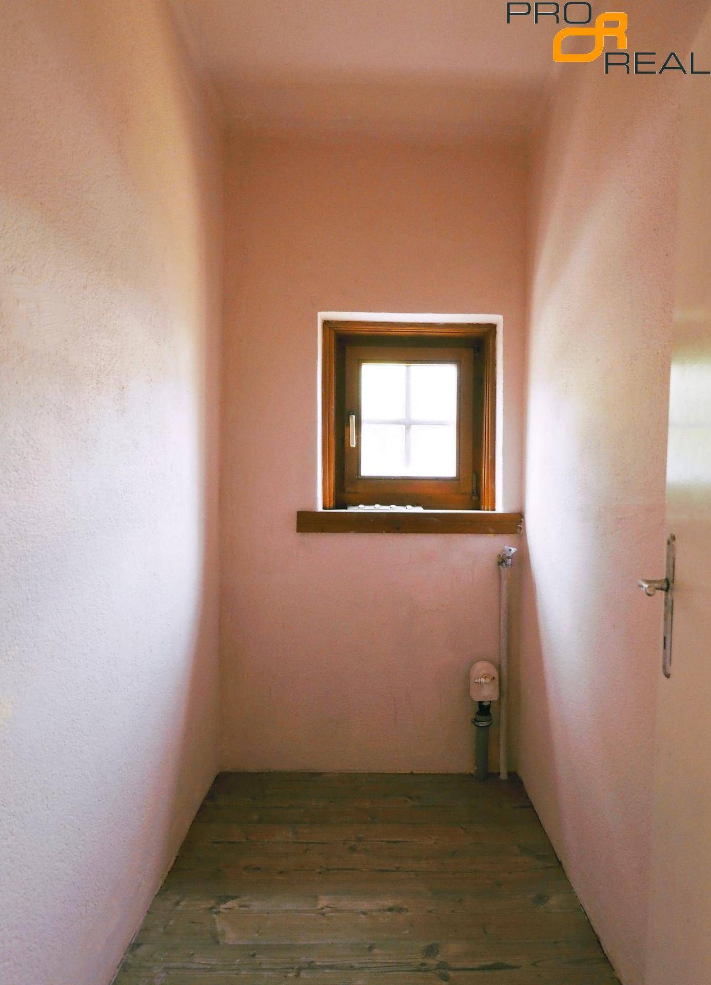 Schmaler Flur mit rosa Wänden, Holzboden und einem kleinen Fenster für natürliches Licht.