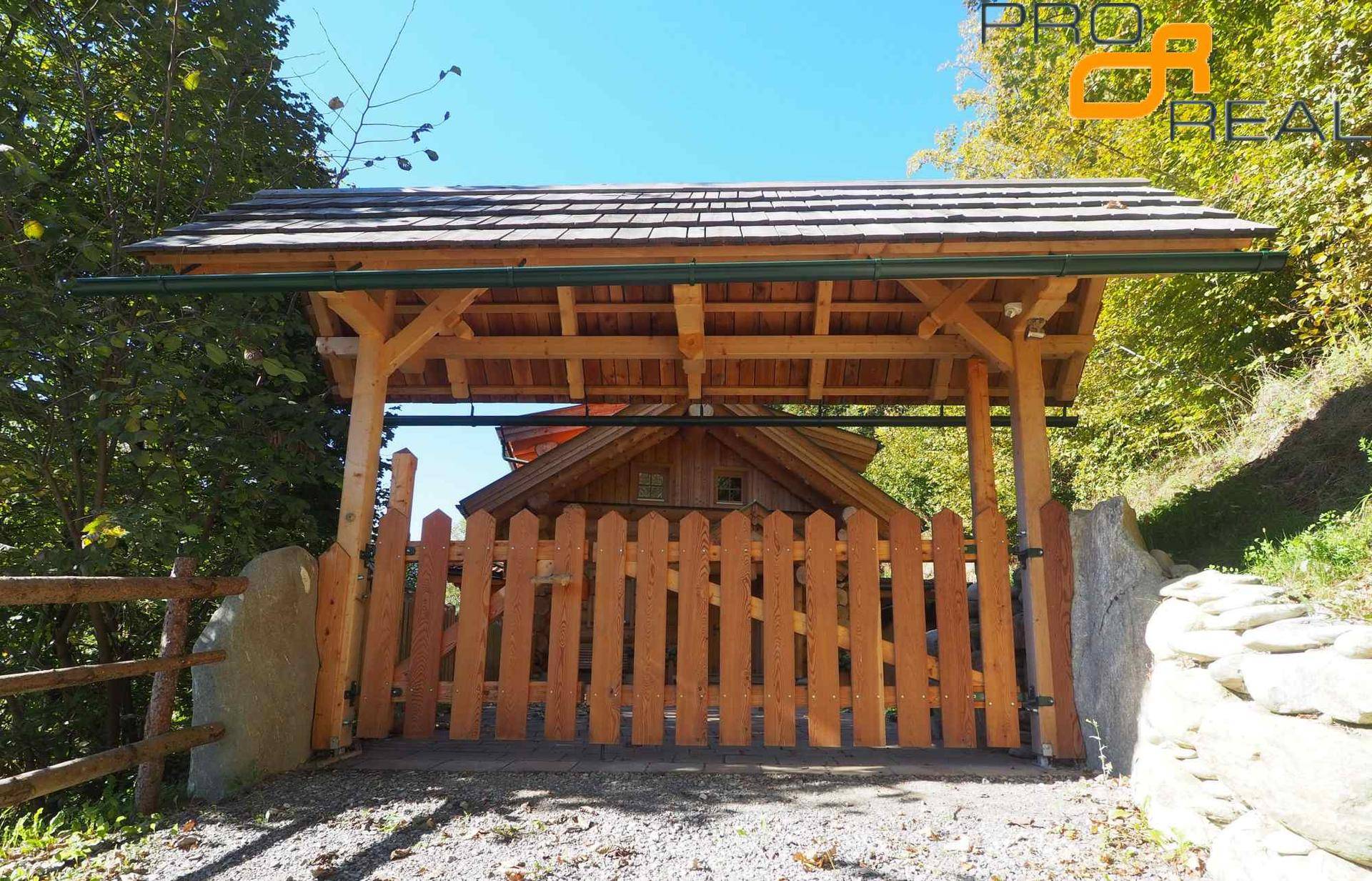 Eingangsbereich mit rustikalem Holzzaun und überdachtem Carport.