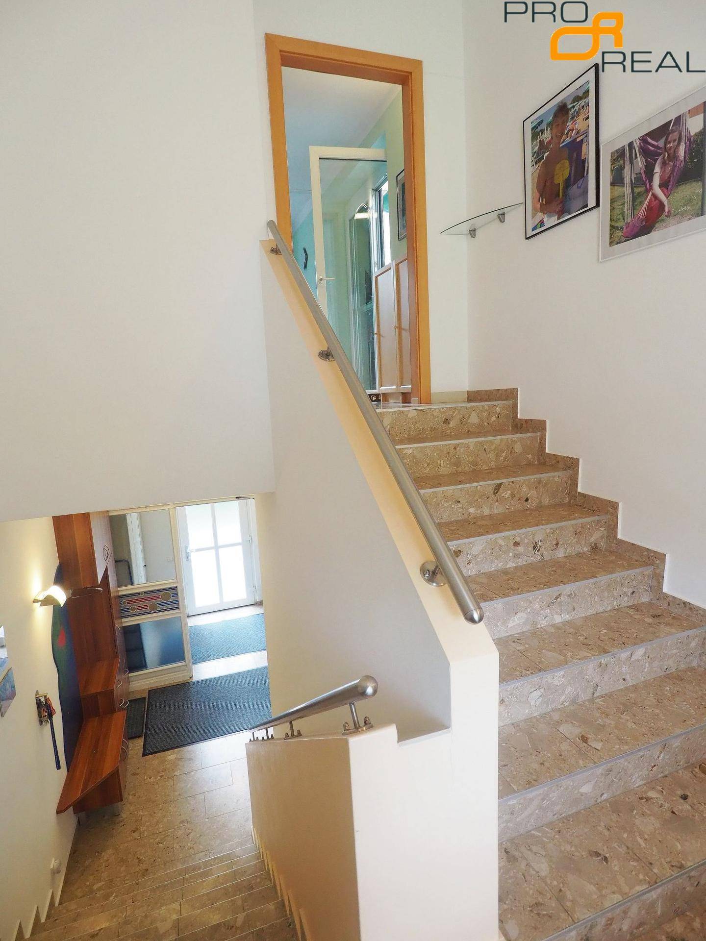 Blick nach oben auf eine elegante Steintreppe mit modernem Metallgeländer und hellem Treppenhaus.