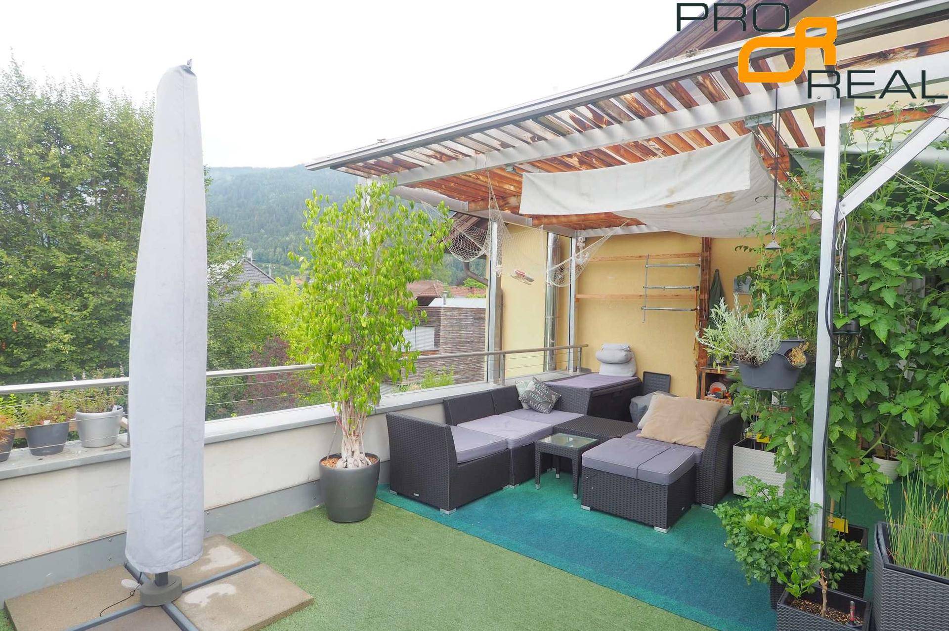 Moderne Terrasse mit Lounge-Möbeln, Sonnenschirm und weitem Blick auf die Berglandschaft.